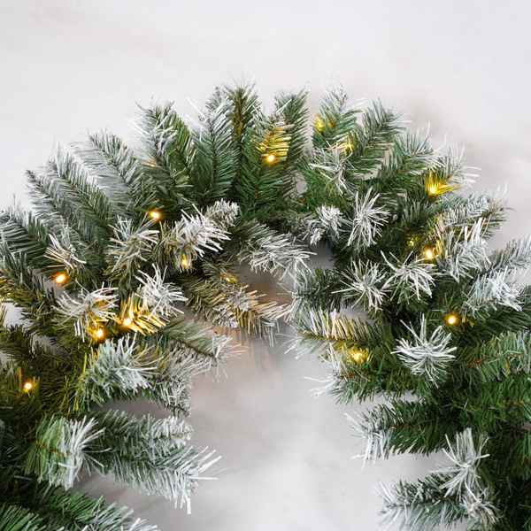 Decorative wreath with greenery and small lights on a white background