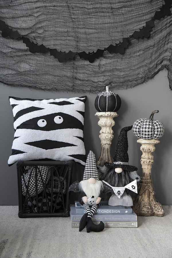 Halloween-themed decor with mummy pillow, gnomes, and pumpkins against a gray wall.