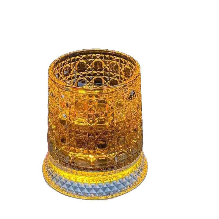 A decorative amber glass tumbler with a textured, faceted pattern and a light blue geometric band at the base, shown on a plain white background.