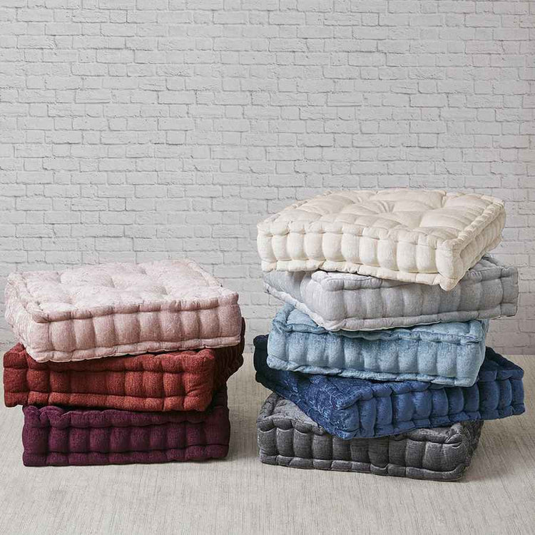 Stacks of quilted seat cushions in various colors against a white brick wall.