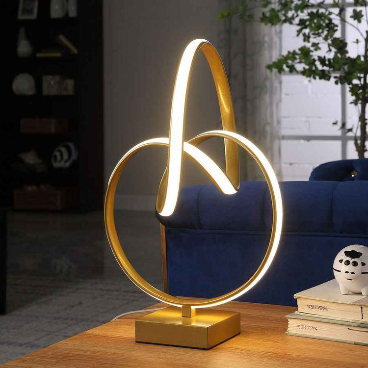 Gold table lamp with circular design on a wooden surface, blurred background of a room.