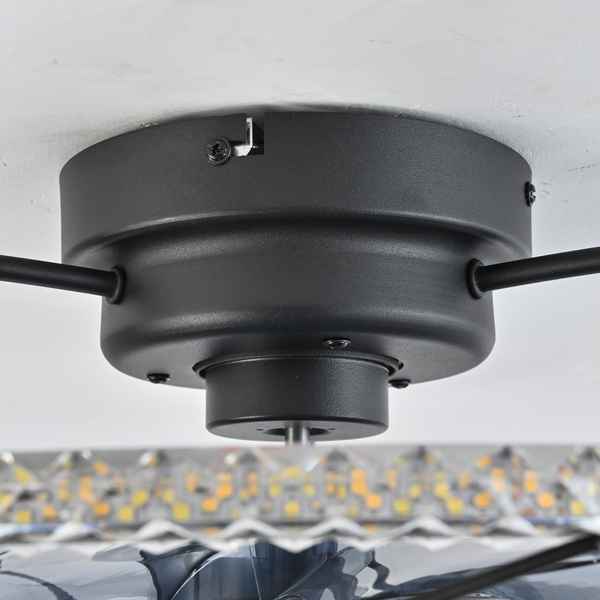 Close-up of a matte black ceiling fan motor housing mounted on a white ceiling, with partial blades visible on both sides and a blurred indoor background below.