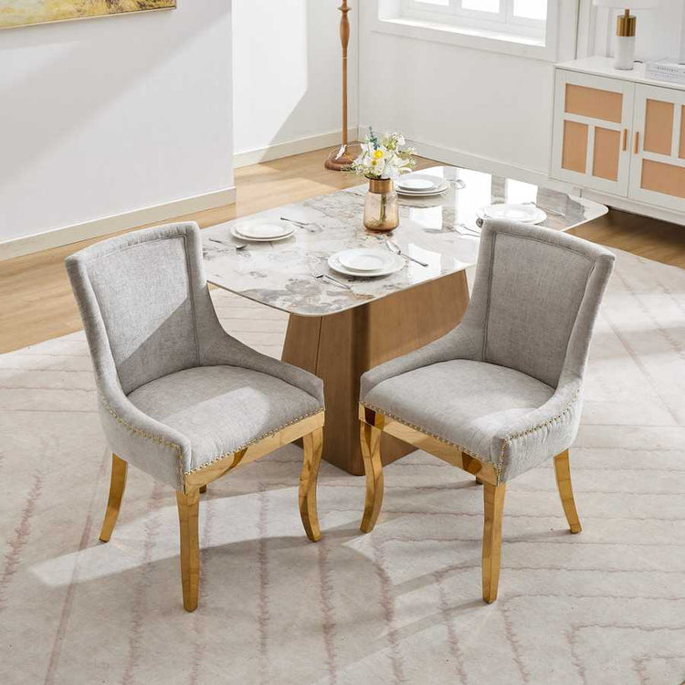 Two gray upholstered chairs with gold legs at a dining table in a room.