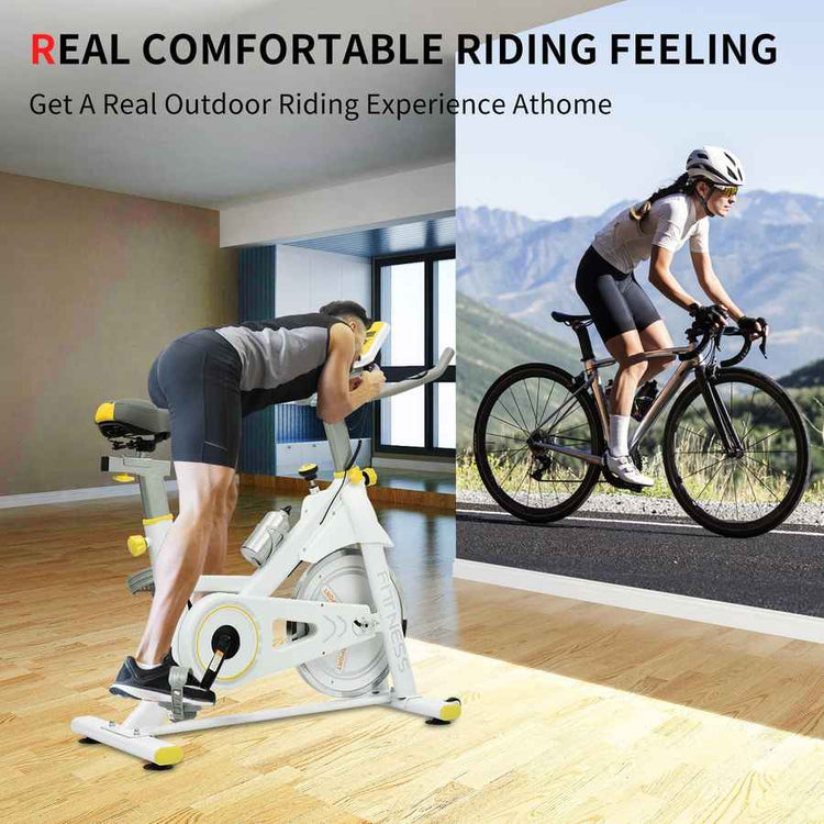 A split promotional image showing a white indoor stationary bike with yellow accents on a wood floor, with a person exercising on it, alongside a woman riding a road bike outdoors on a mountain road. Text at the top reads &