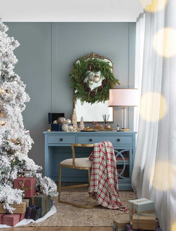 Decorated living room with Christmas tree, wreath, and gifts against a blue wall.
