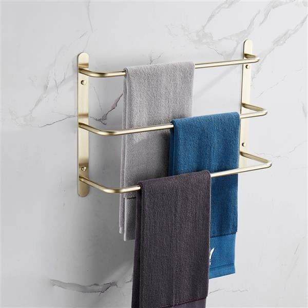 Gold wall-mounted towel rack with three colorful towels on marble bathroom wall