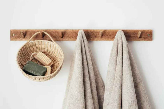 Wooden wall rack with beige towels and a wicker basket holding soap and a brush