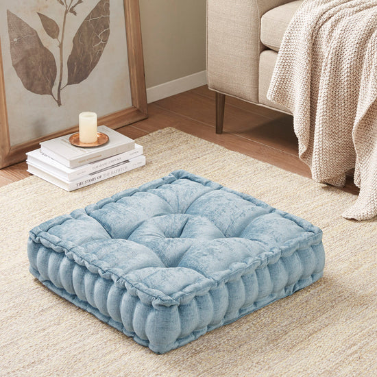 Blue cushion on a beige carpet with a candle and books in the background