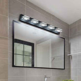 A modern bathroom vanity light fixture with four rectangular LED light heads mounted above a large rectangular mirror with a black frame, set against a gray tiled wall.