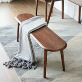 Wooden bench with a gray blanket draped over it on a patterned rug.