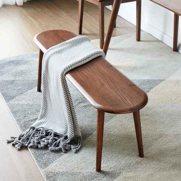 Wooden bench with a gray blanket draped over it on a patterned rug.