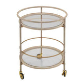 A two-tier round bar cart with a champagne gold metal frame, clear glass shelves, and gold caster wheels, shown on a solid white background.