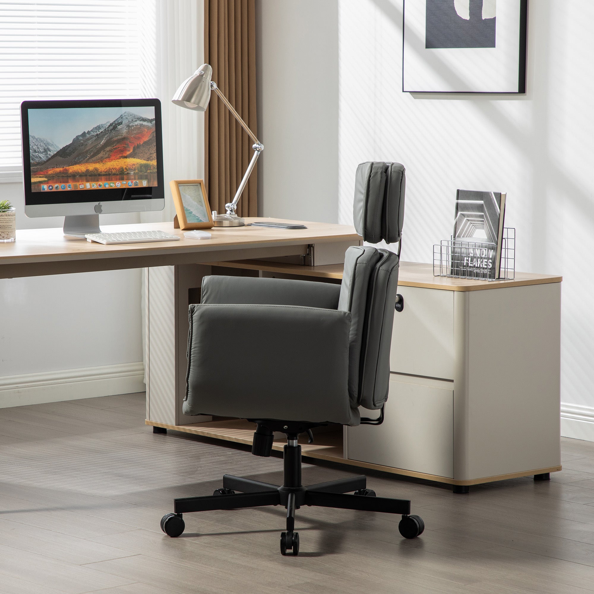 Modern office desk with computer, lamp, and gray office chair in a bright room.