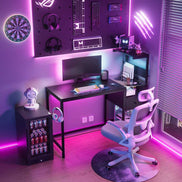 Gaming setup with black computer desk featuring USB ports, power outlet, and reversible shelves, illuminated by purple LED lights.