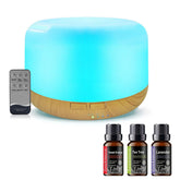A cylindrical LED ultrasonic diffuser with a glowing blue light and a natural wood base, shown with a black remote control and three essential oil bottles labeled Sweet Orange, Tea Tree, and Lavender on a white background.