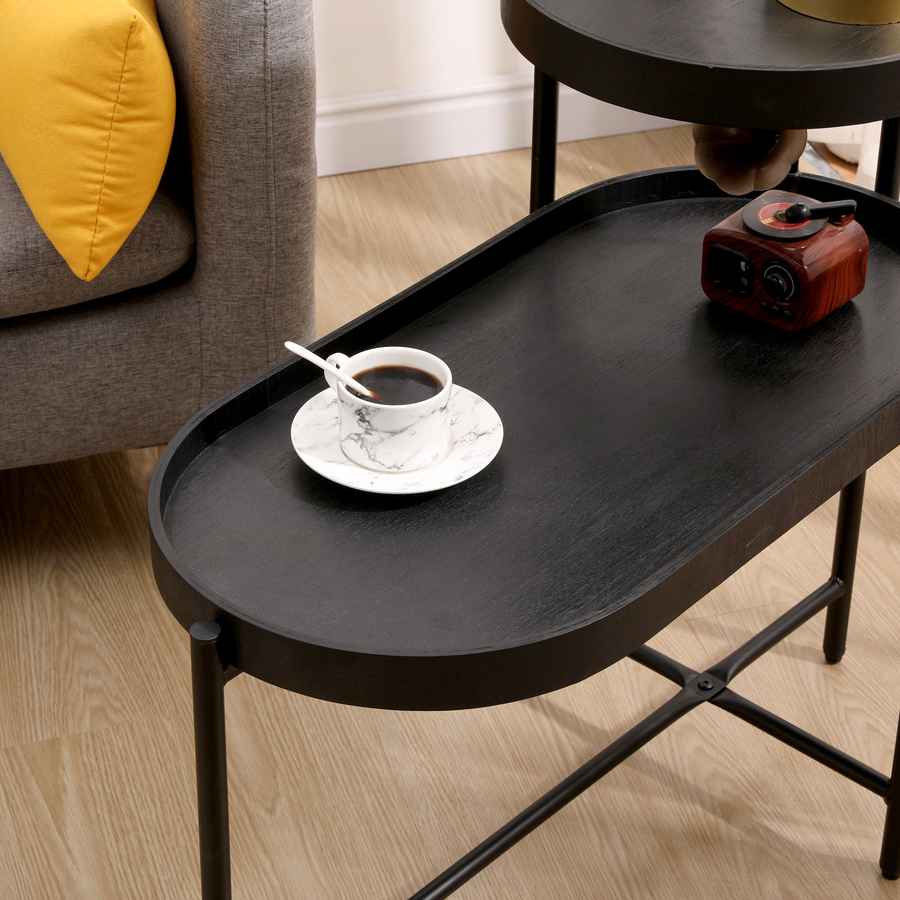 Black side table with a cup of coffee on a saucer in a living room setting.