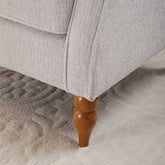 Close-up of a gray upholstered chair with a wooden leg on a textured beige carpet.
