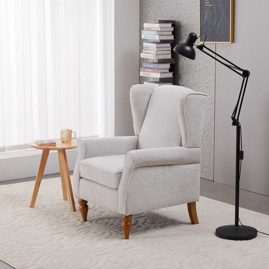 Gray armchair in a room with a side table, lamp, and books.