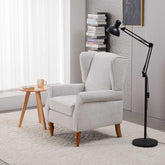 Gray armchair in a room with a side table, lamp, and books.