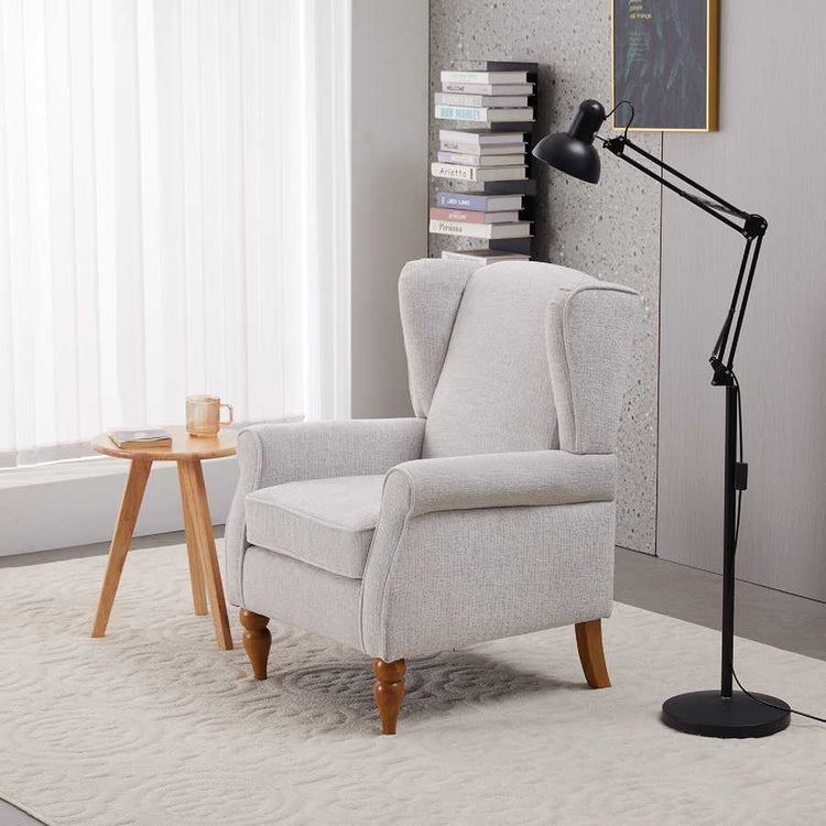 Gray armchair in a room with a side table, lamp, and books.