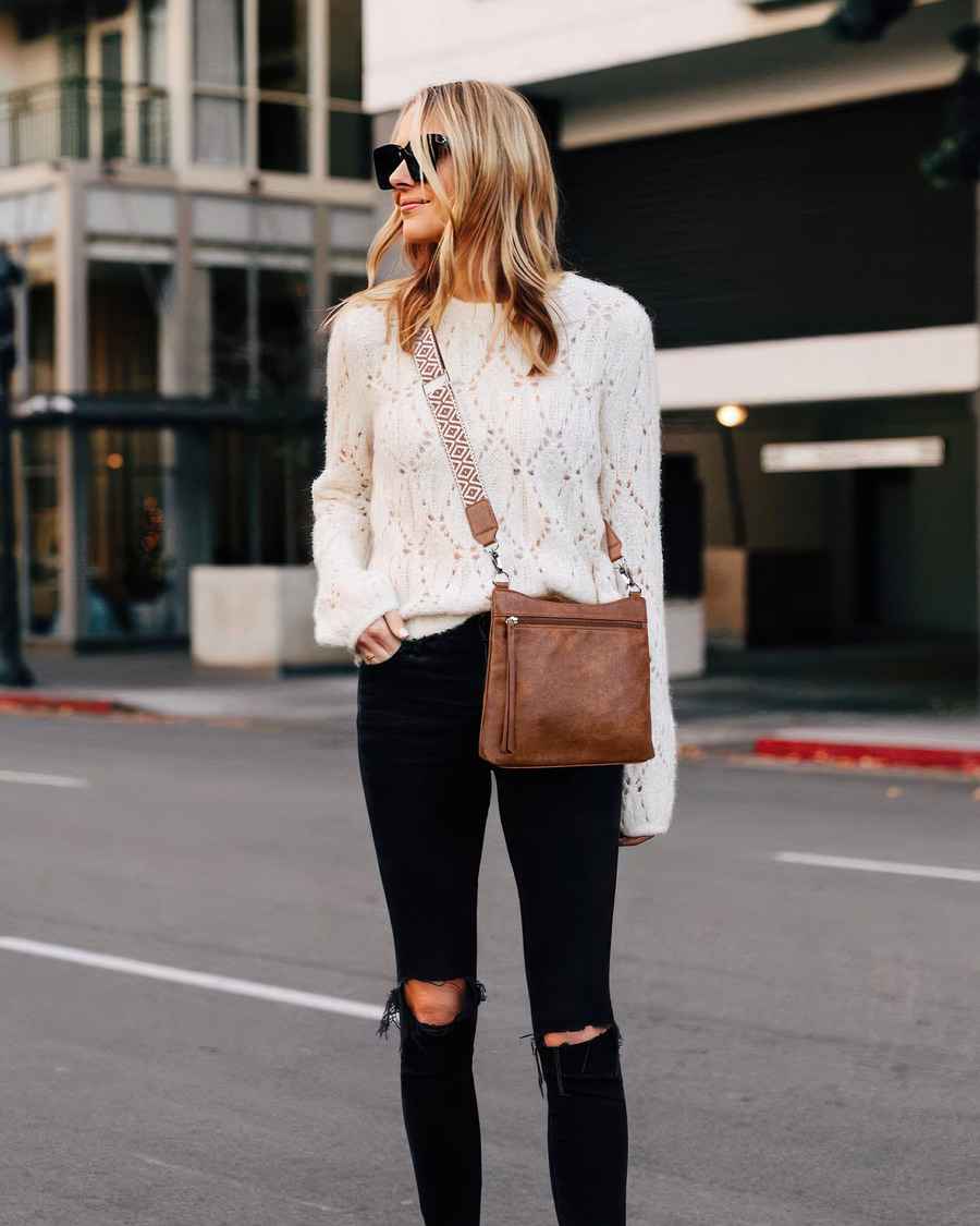 Woman in a white lace sweater and black pants walking on a city street.