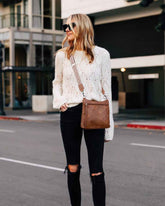 Woman in a white lace sweater and black pants walking on a city street.