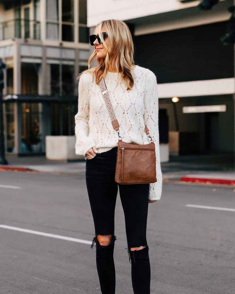 Woman in a white lace sweater and black pants walking on a city street.