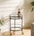 Bar cart with a bottle of whiskey and glasses in a room with a plant and sofa.