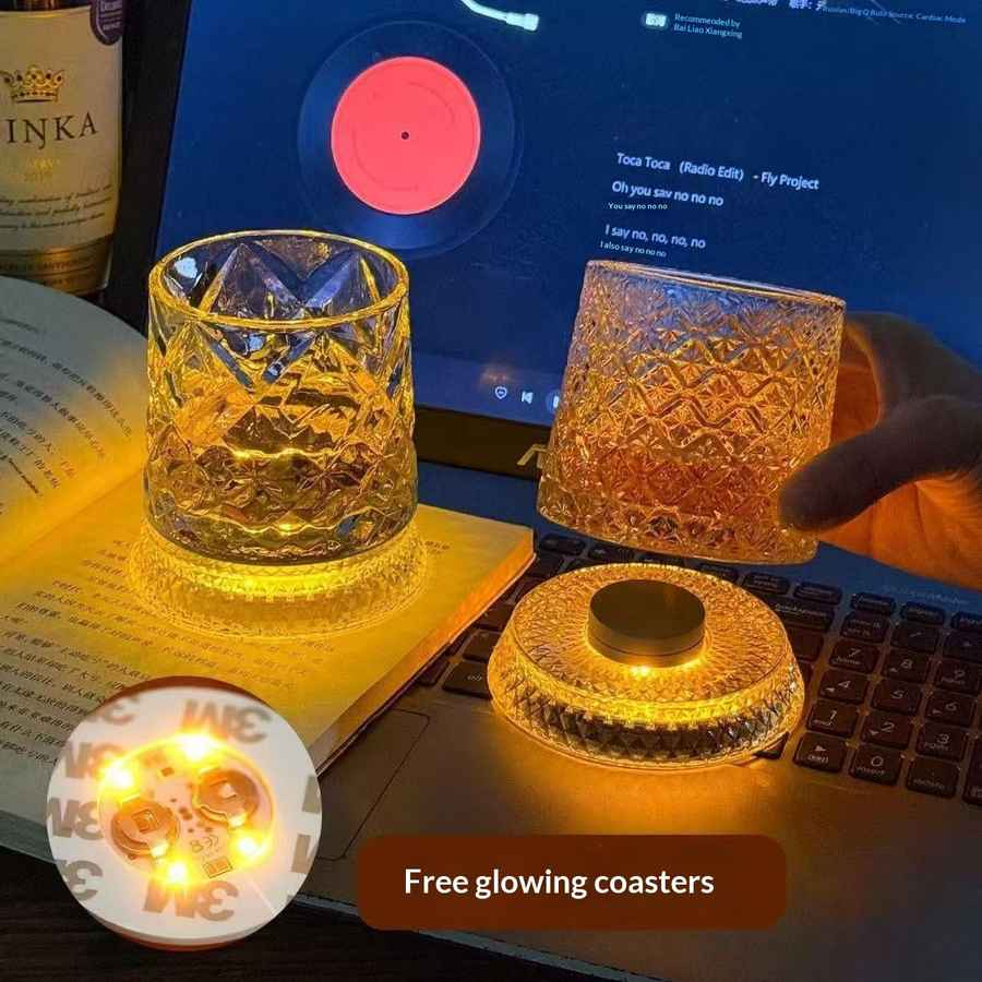 A set of glowing whiskey glasses with built-in LED light strips, shown on a laptop and held by a hand. The glasses emit a warm yellow light, and a circular inset shows the back of one glass with its light strip.