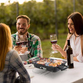 People enjoying a barbecue outdoors with wine glasses.