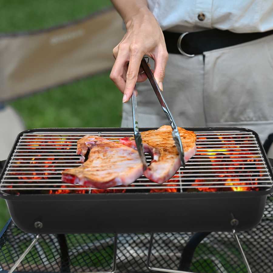 Person grilling fish on a portable barbecue grill outdoors.