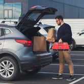 Man loading groceries into a car trunk in a parking lot