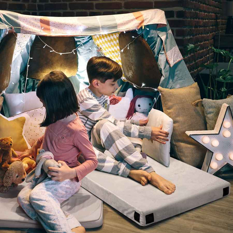 Children playing on a small bed with pillows and blankets in a cozy room.