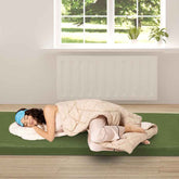 Person lying on a yoga mat with a blanket and eye mask in a bright room with a window.