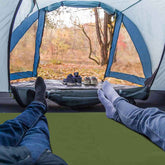 Person inside a tent looking out at a forest with shoes on the ground