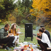 Group of people having a picnic with a portable barbecue in a forest setting.