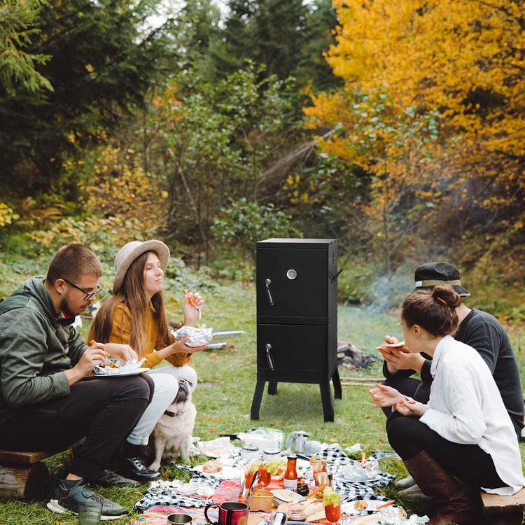 Group of people having a picnic with a portable barbecue in a forest setting.