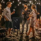 People socializing outdoors at night with string lights and a portable stove.