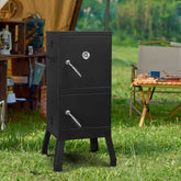 Black metal smoker grill on grass with camping setup in the background