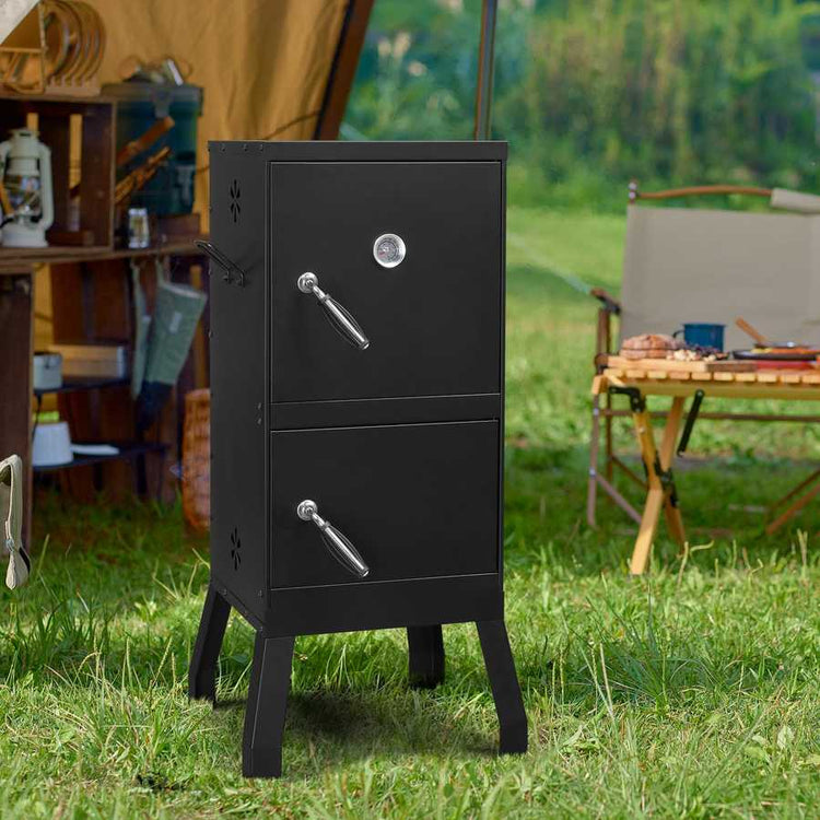 Black metal smoker grill on grass with camping setup in the background