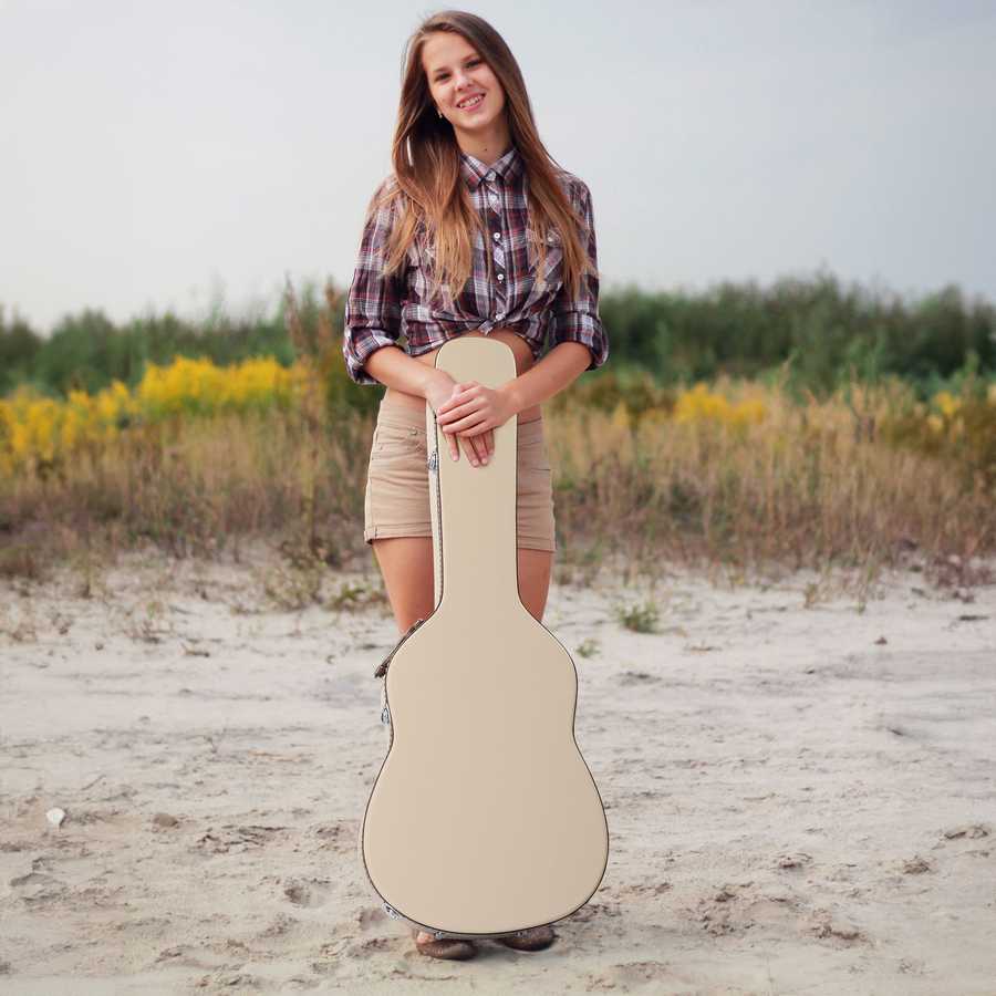 Woman holding a guitar case in a natural setting with yellow flowers and greenery.