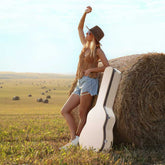 Woman with a guitar case standing next to a hay bale in an open field