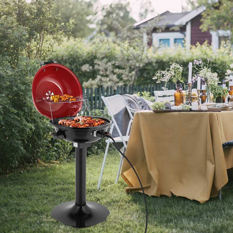 Outdoor setting with a red portable grill and a table with food and drinks in a garden.