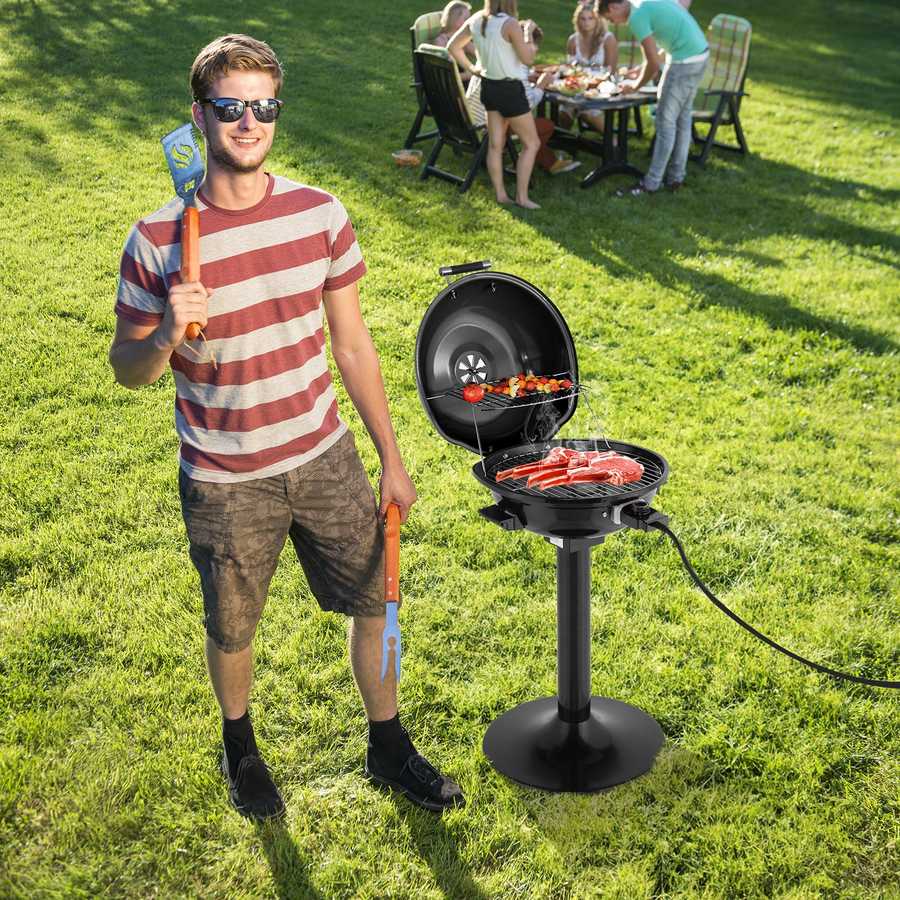 Man holding a spatula and standing next to a portable grill with people in the background