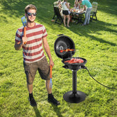 Man holding a spatula and standing next to a portable grill with people in the background