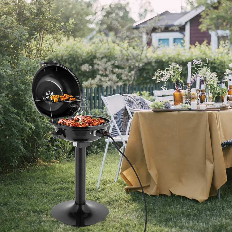 Outdoor grill with food on a grassy area next to a table with drinks and snacks.