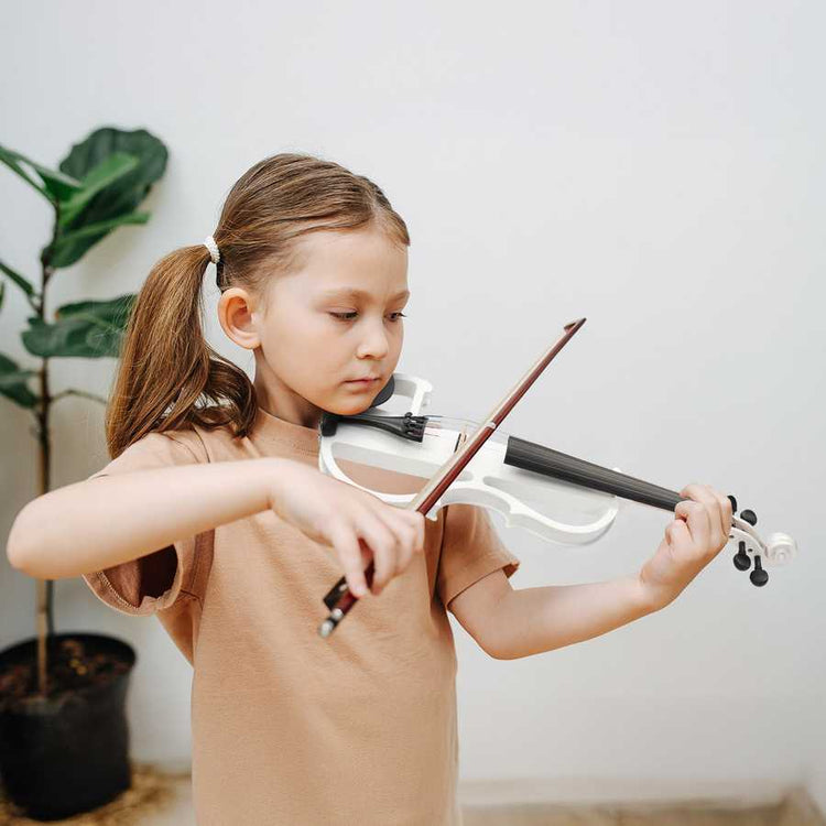 Young girl playing violin indoors with a plant in the background