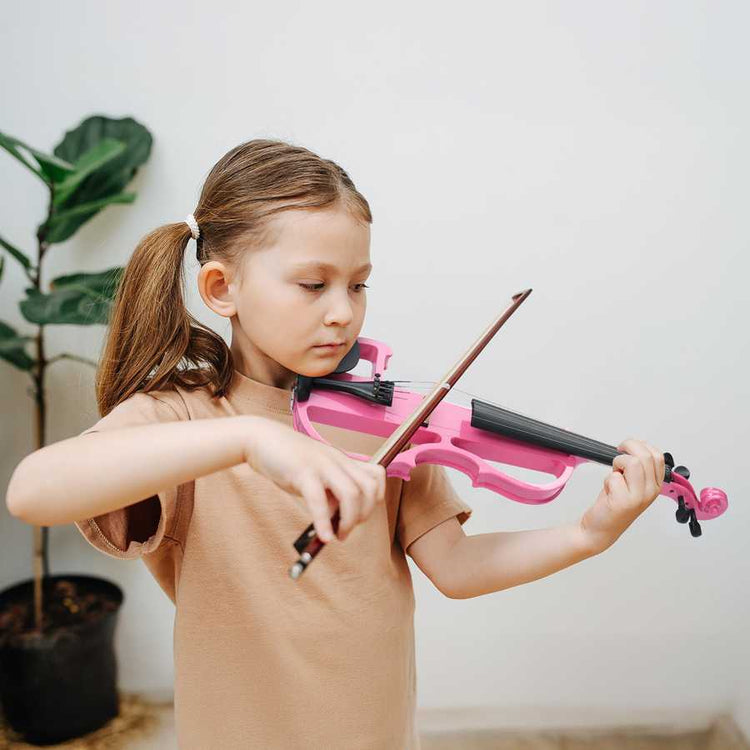 Young girl playing a pink violin indoors with a plant in the background