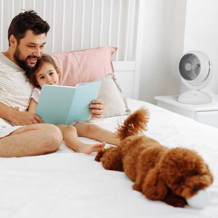 Family using portable desk fan in bedroom with pet and white furniture
