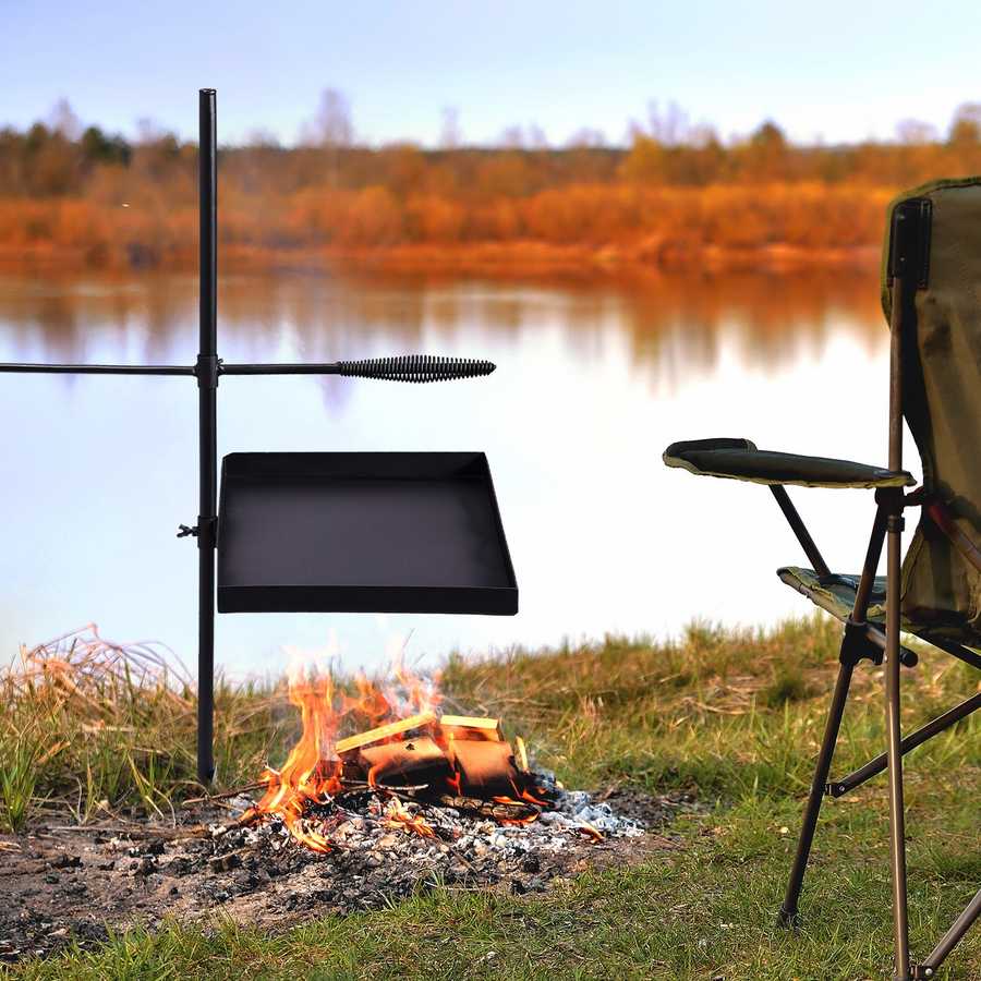 Outdoor cooking setup with a grill over a campfire by a lake